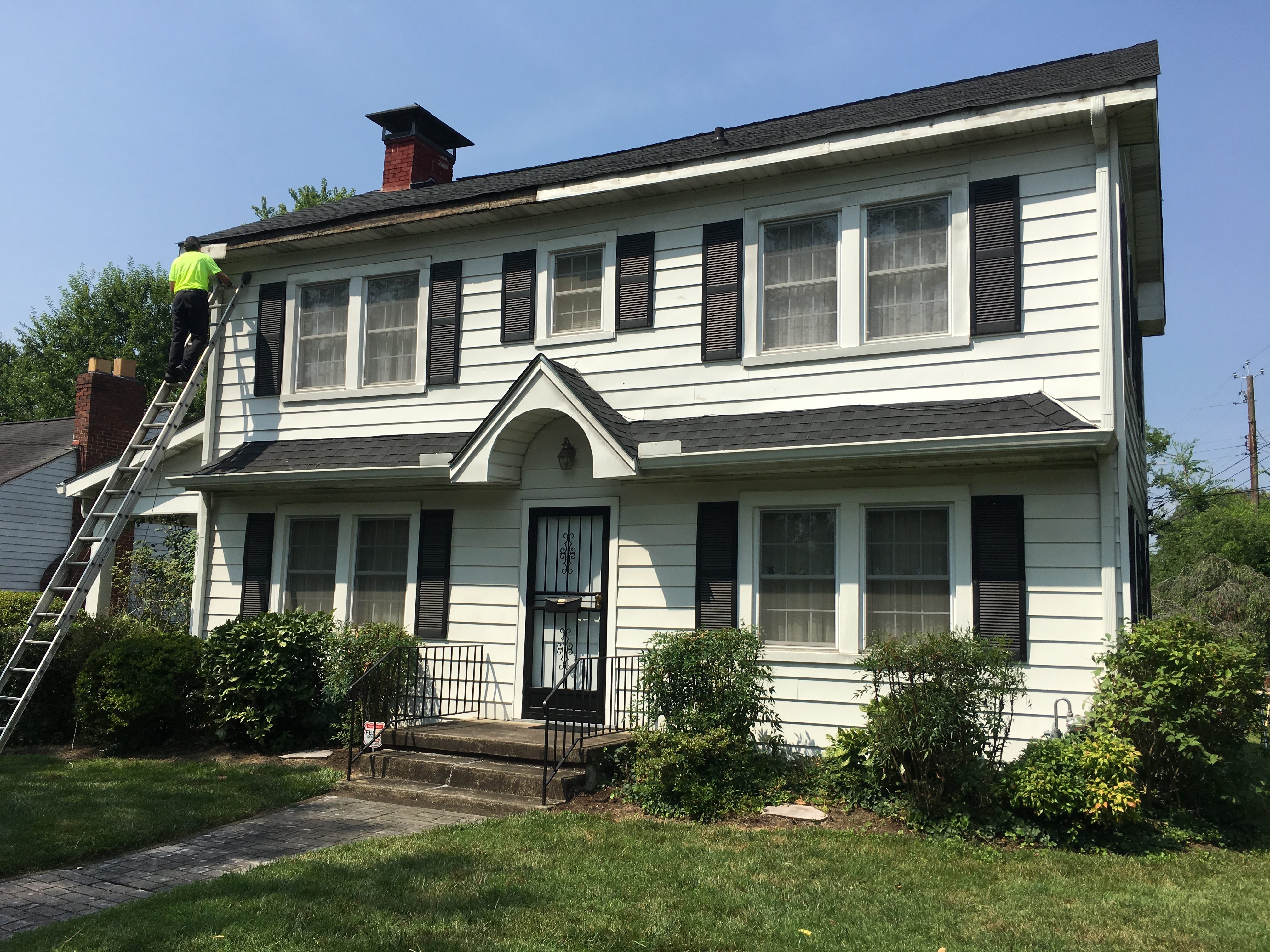 after removing gutter and aluminum fascia wrap, this image shows a worker on the ladder exposing decayed fascia wood