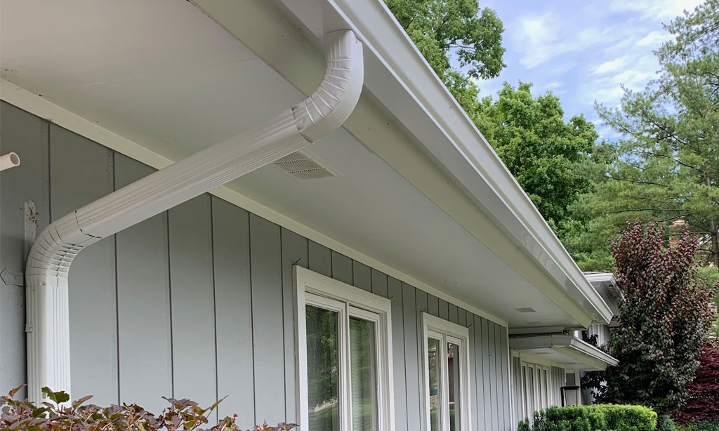 6-inch white gutters with 4x3 inch downspouts installed on a grey home with batten board siding