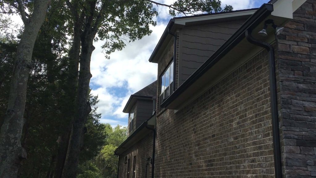 looking skyward at 5-inch black gutters with leaf lock gutter guards installed. The gutters are on the rear of a garage under the canopy of oak trees in Nolensville Tennessee
