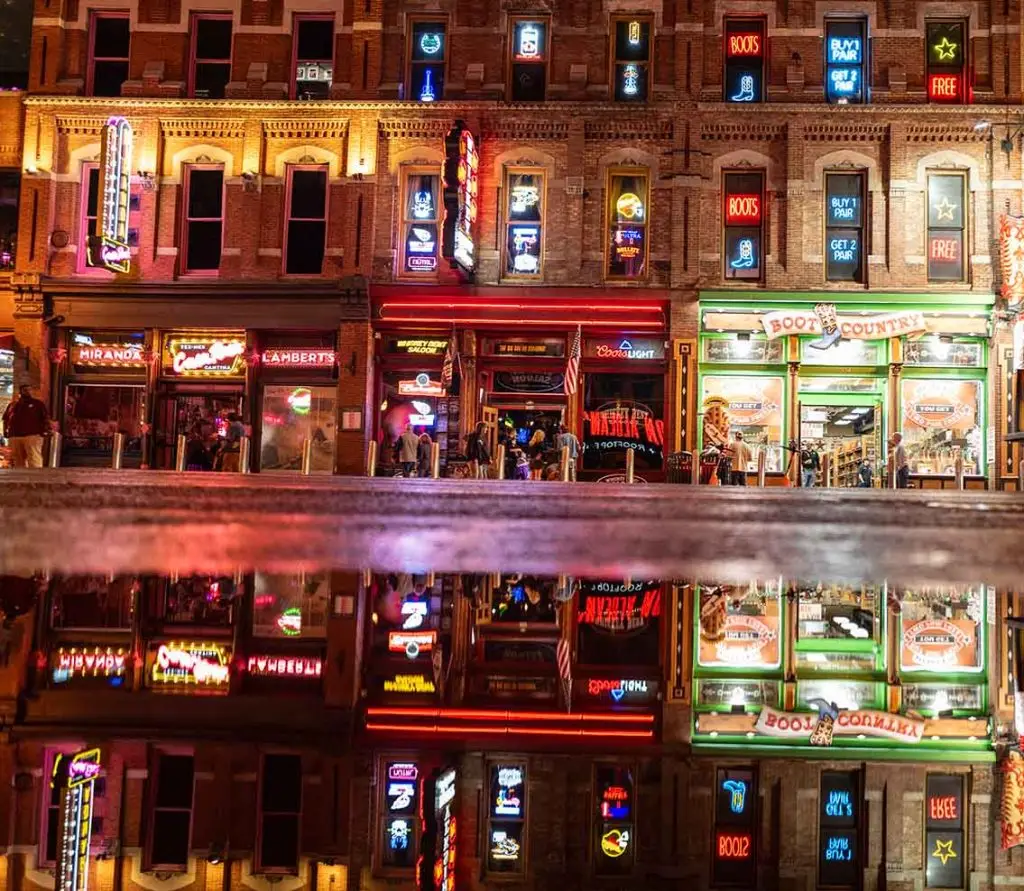 boot country, located in downtown nashville, Tennessee, offers buy 1 get 2 free pair of boots. photo taken by Johnathan Skardon shows the reflection of boot country and two other bars in a puddle on broadway avenue at nighttime